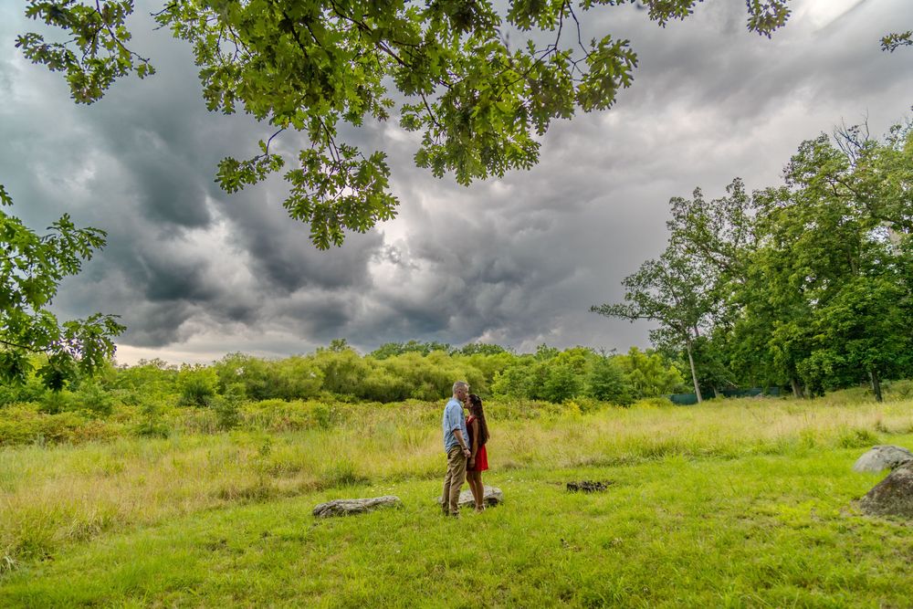 Person standing in green field under dramatic stormy sky with dark clouds rolling in over lush trees.