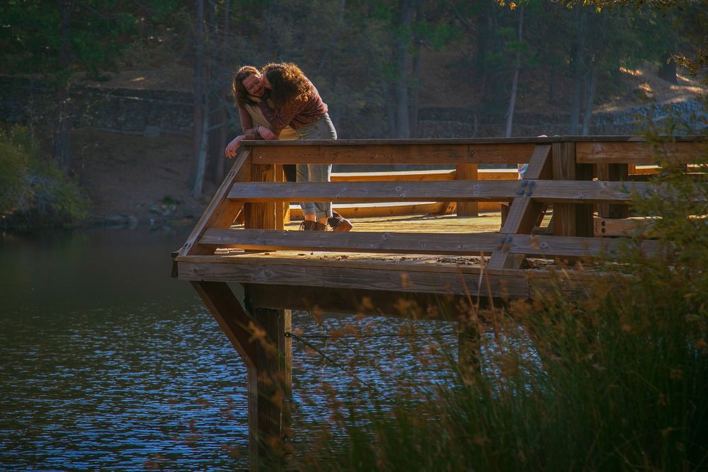 Bear sitting on wooden dock at sunset overlooking peaceful lake.