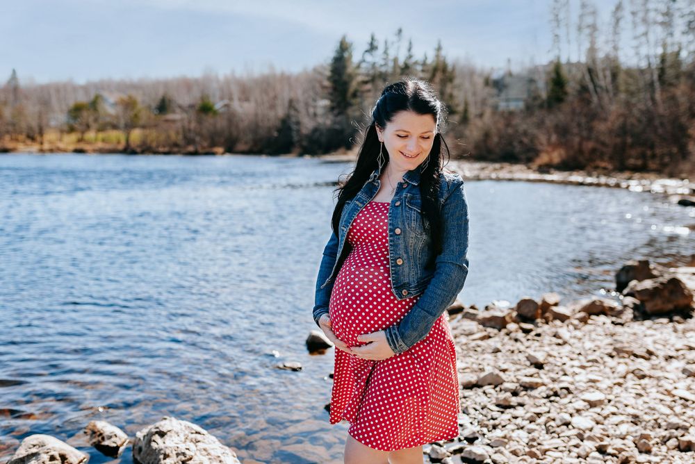 Couple sharing tender moment during maternity shoot by rocky waterfront.