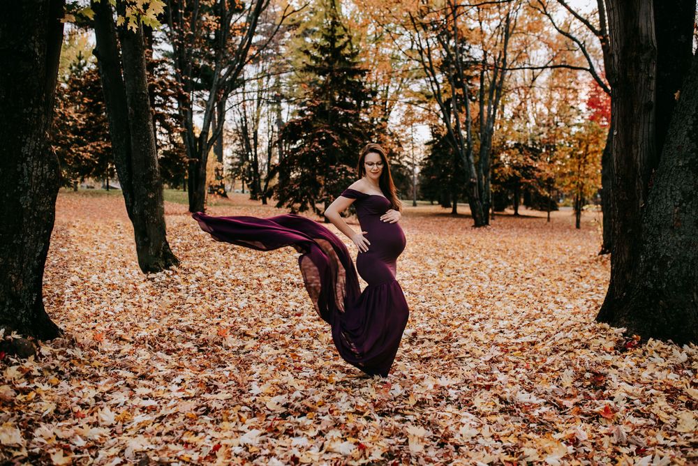 Flowing purple dress maternity photo with dress movement in autumn forest setting.