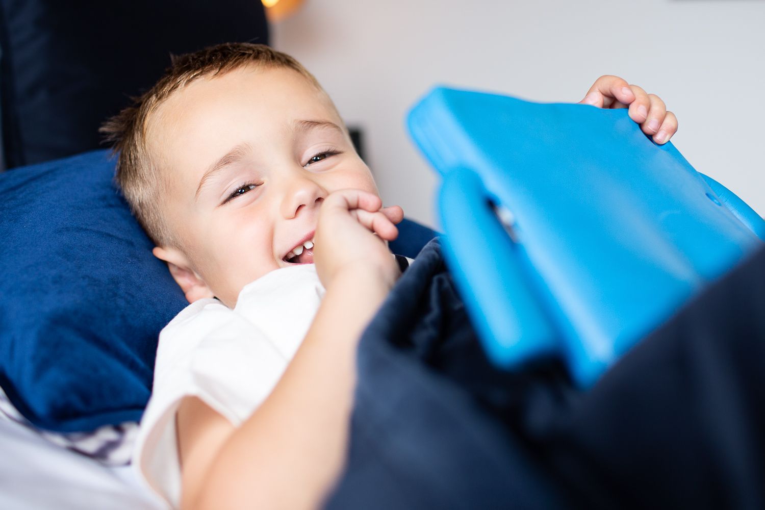 A small child experiencing laughter while laying on a blue pillow.