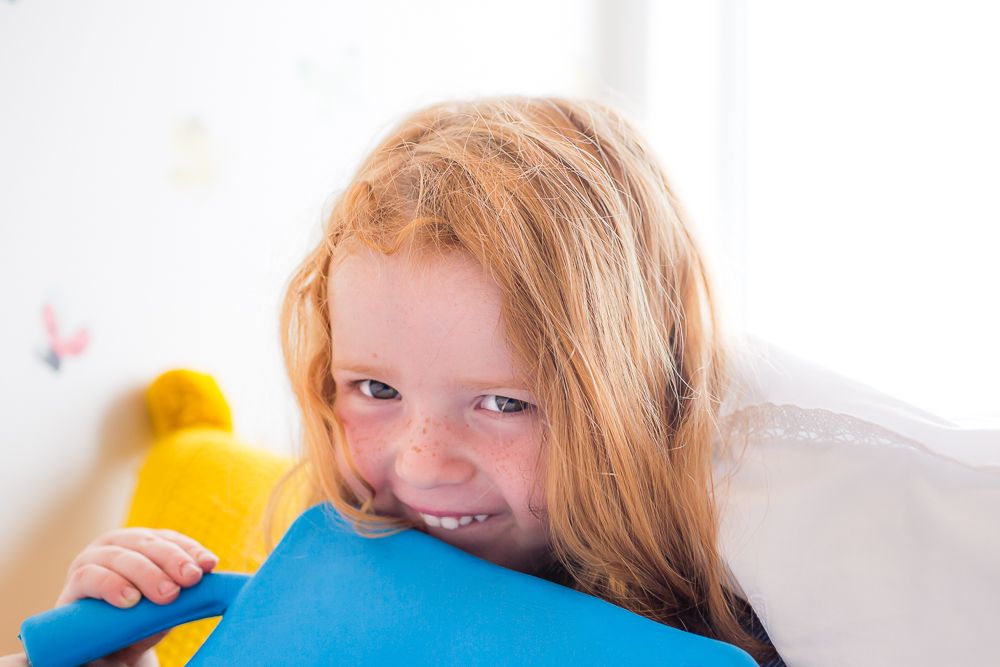 A child with red hair smiles while hugging a blue pillow.