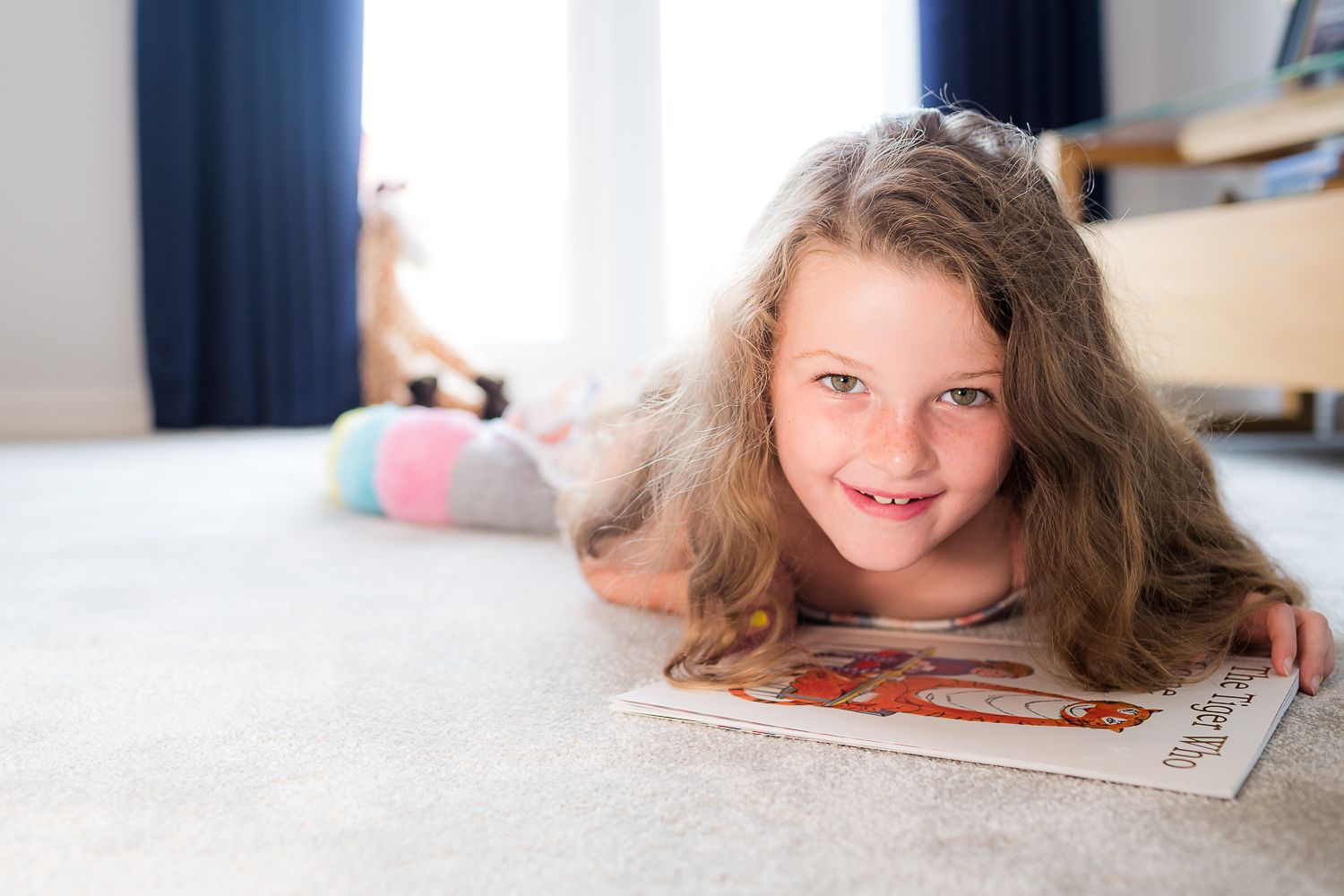 A smiling child lies on carpet while reading a book.