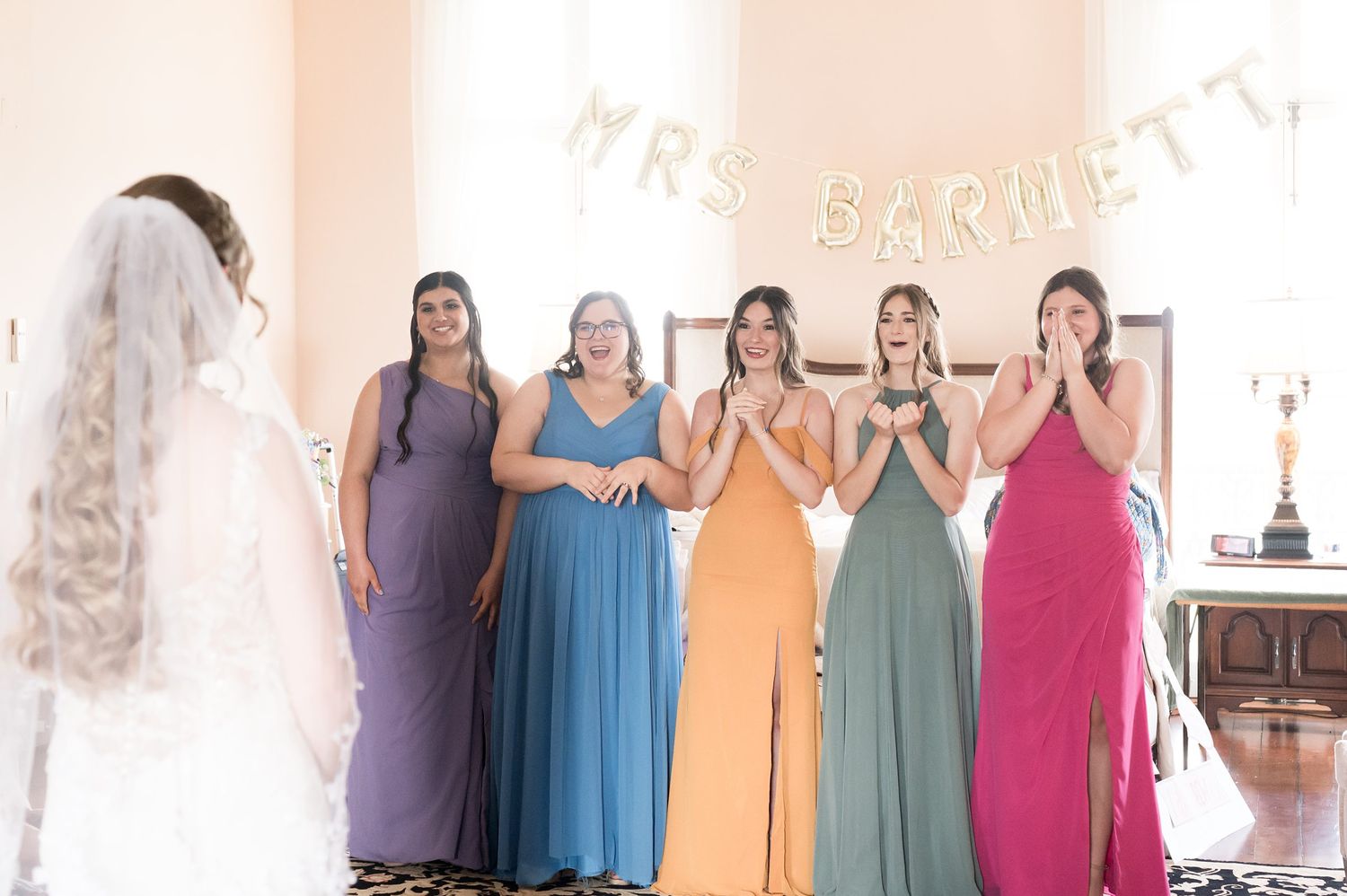 Bridesmaids in different colored dresses stand in a row at a wedding venue.