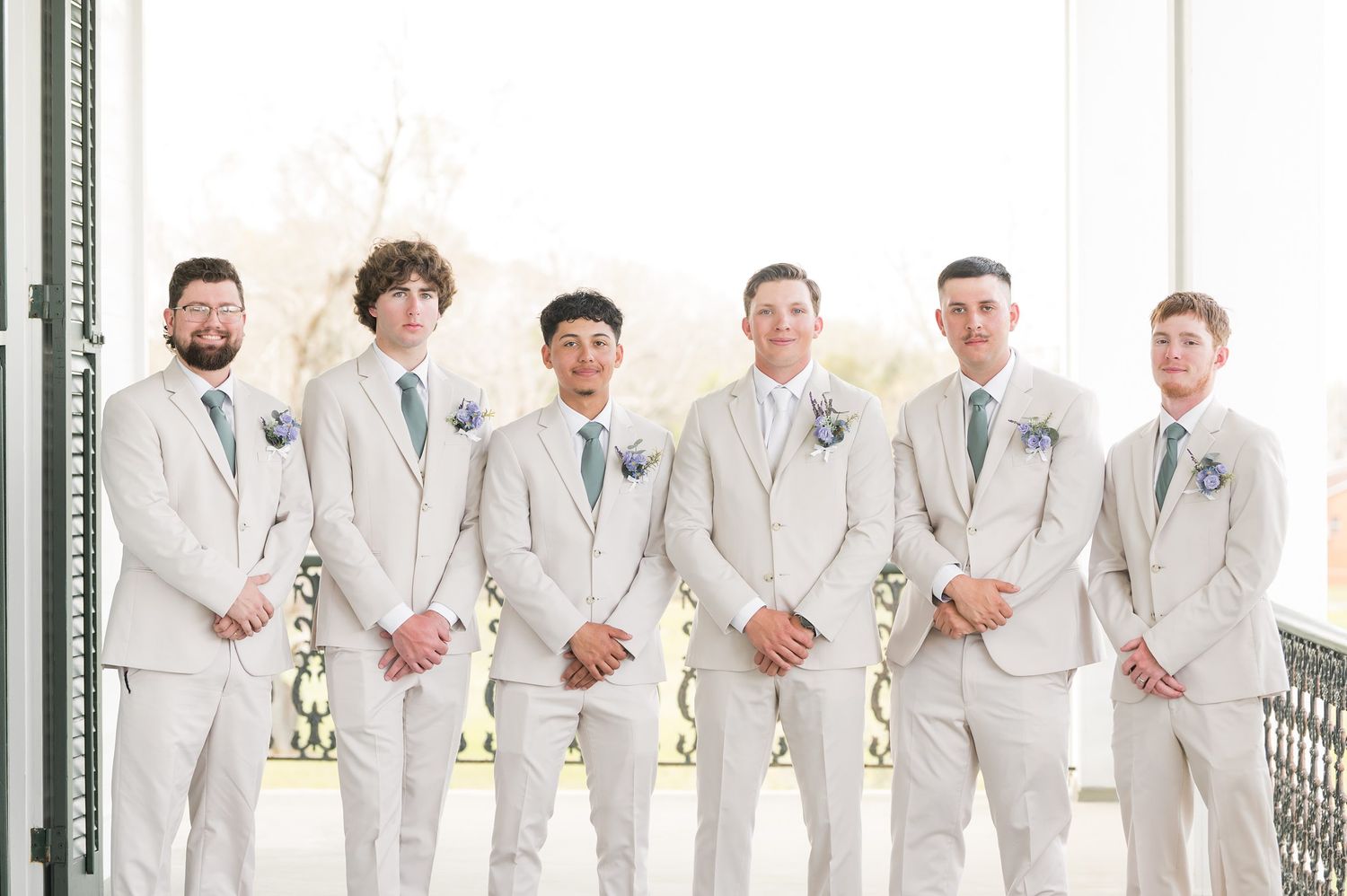 Wedding party members in light colored suits stand in a formal line.