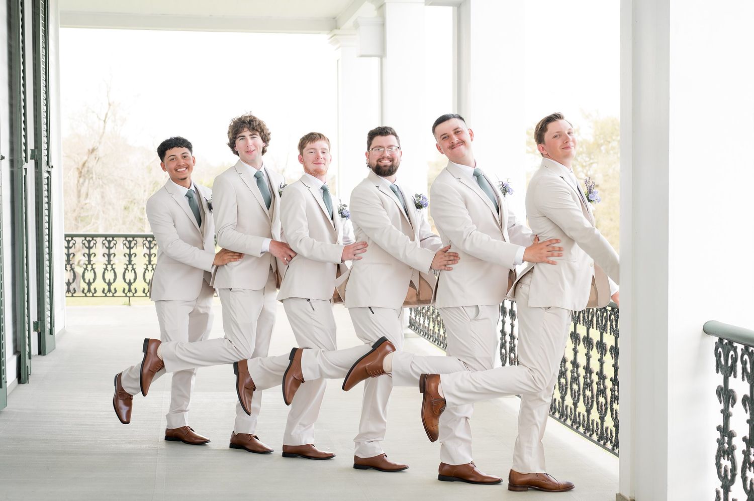 Groomsmen in white suits strike a fun pose on stairs.