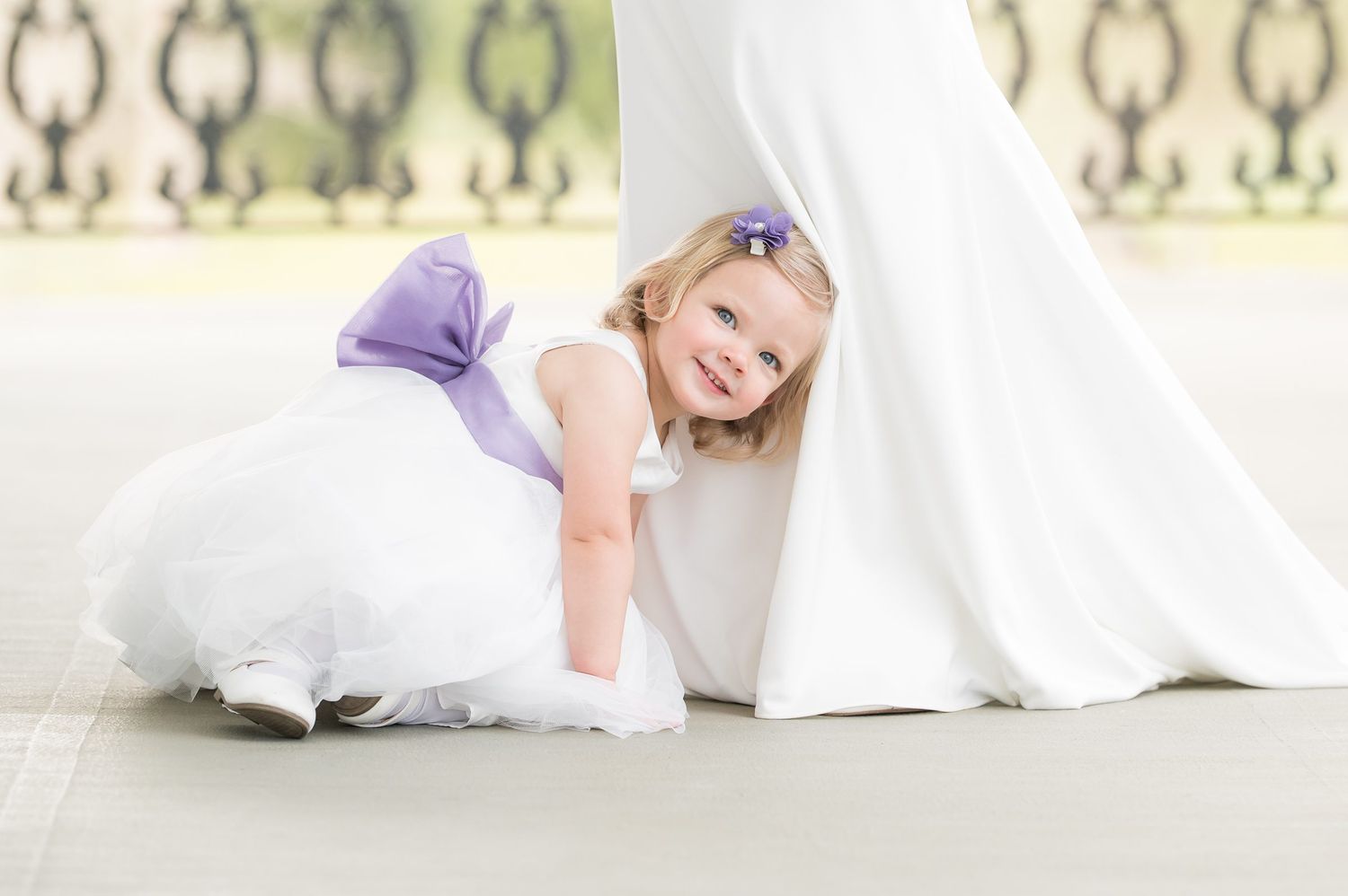 A bride in a flowing white wedding dress lies on a white couch while reading a book.
