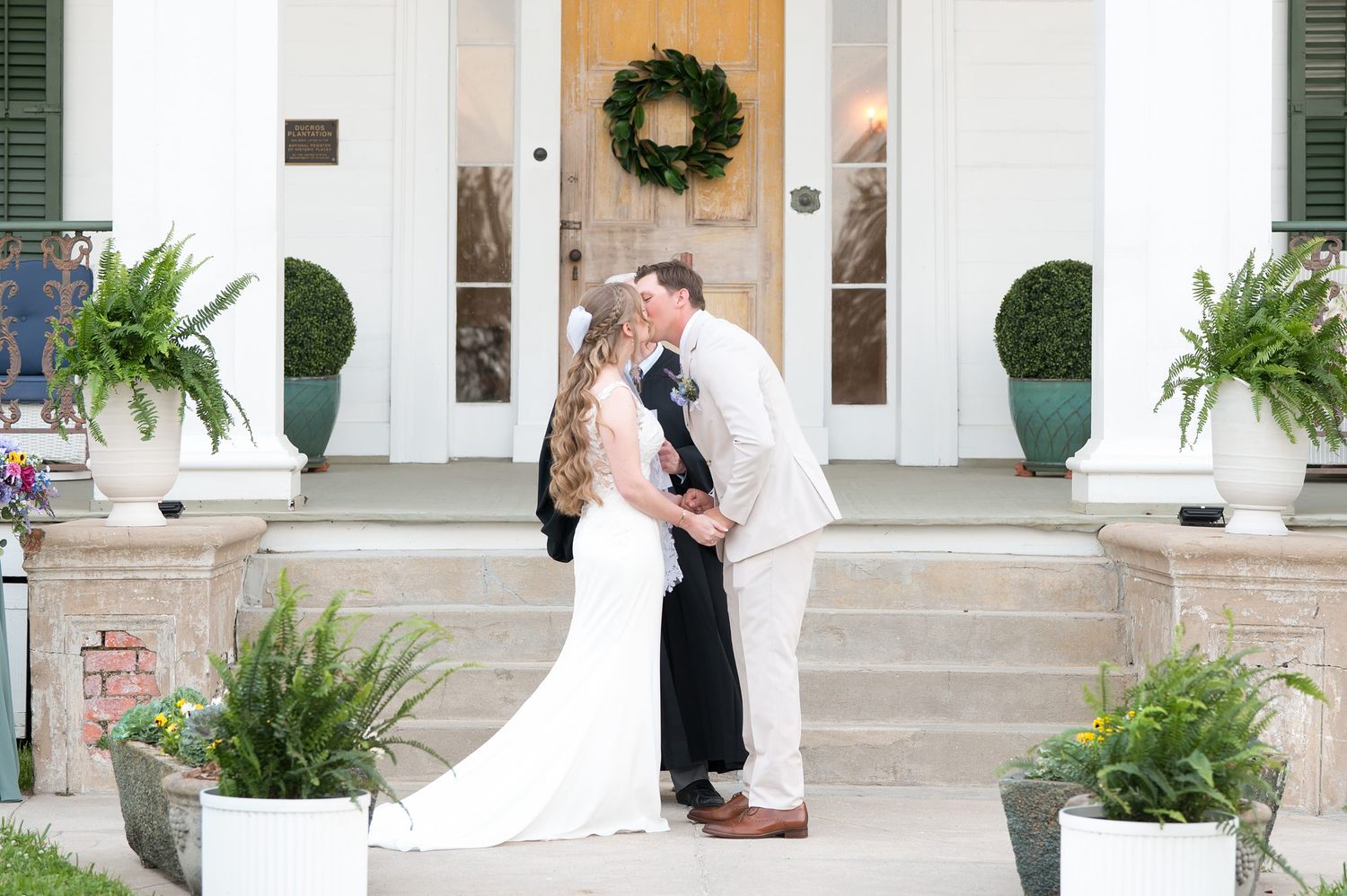 Romantic wedding scene on plantation home steps with potted ferns and holiday wreath decor.