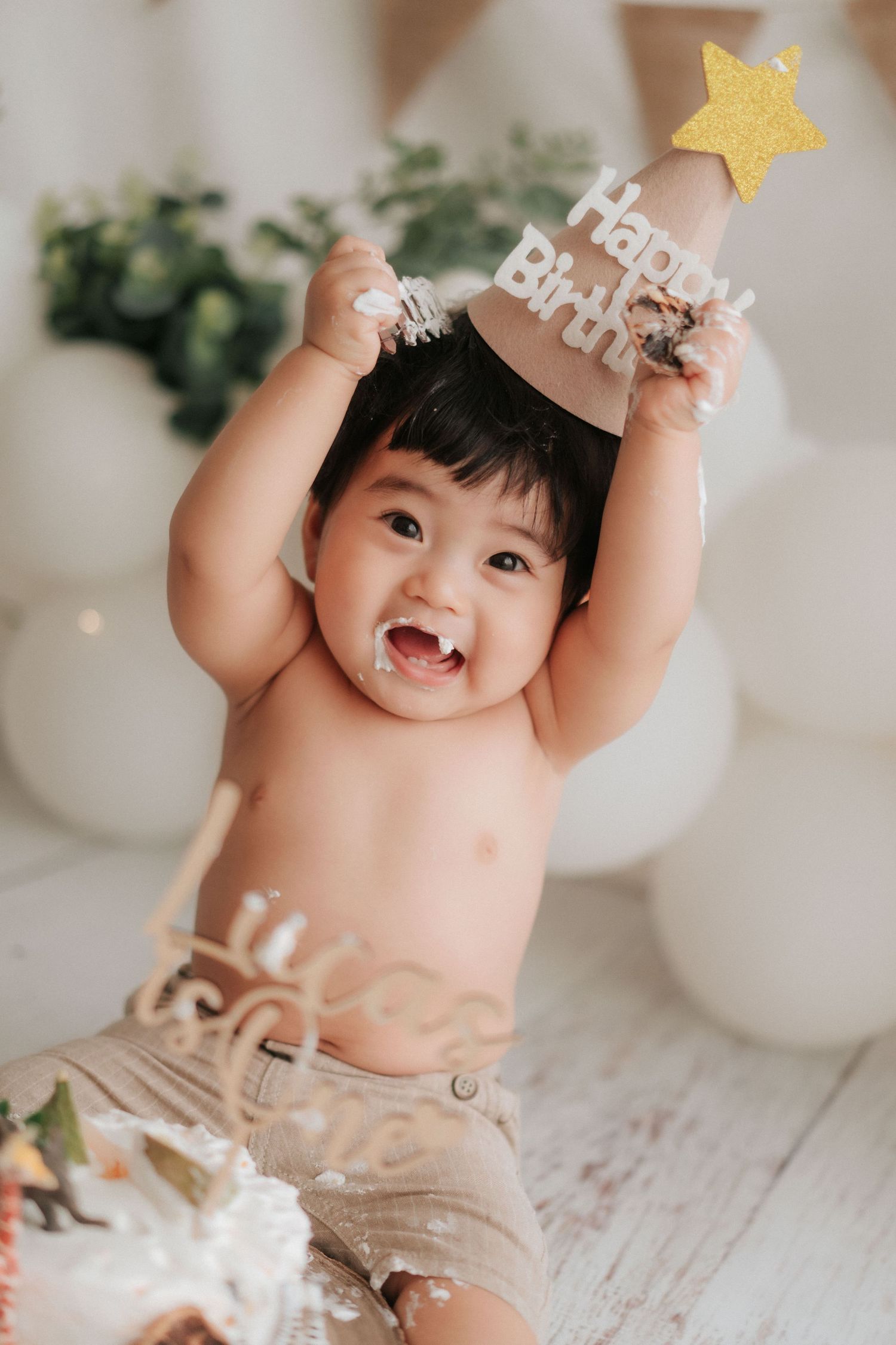A baby sits on a white surface with a festive birthday cake display featuring decorative elements.一個嬰兒坐在白色的表面上,旁邊擺放著一個裝飾精美的生日蛋糕。