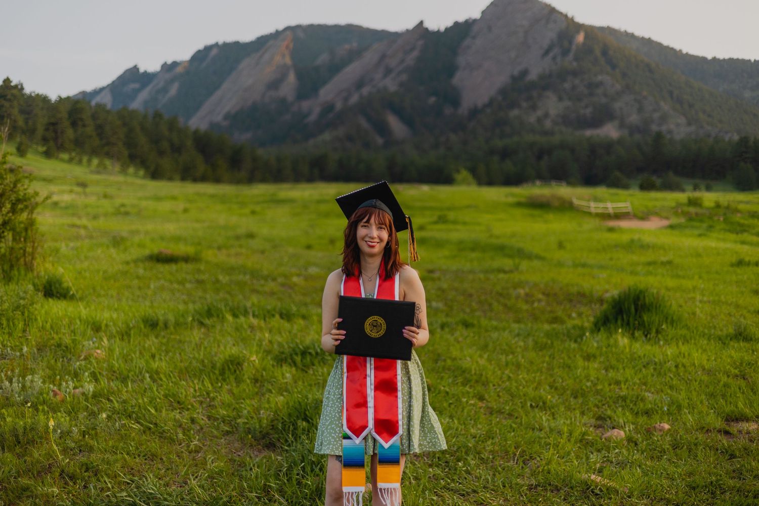CU Denver graduate in cap and gown posing in front of the iconic front range mountains in Aurora, Colorado.