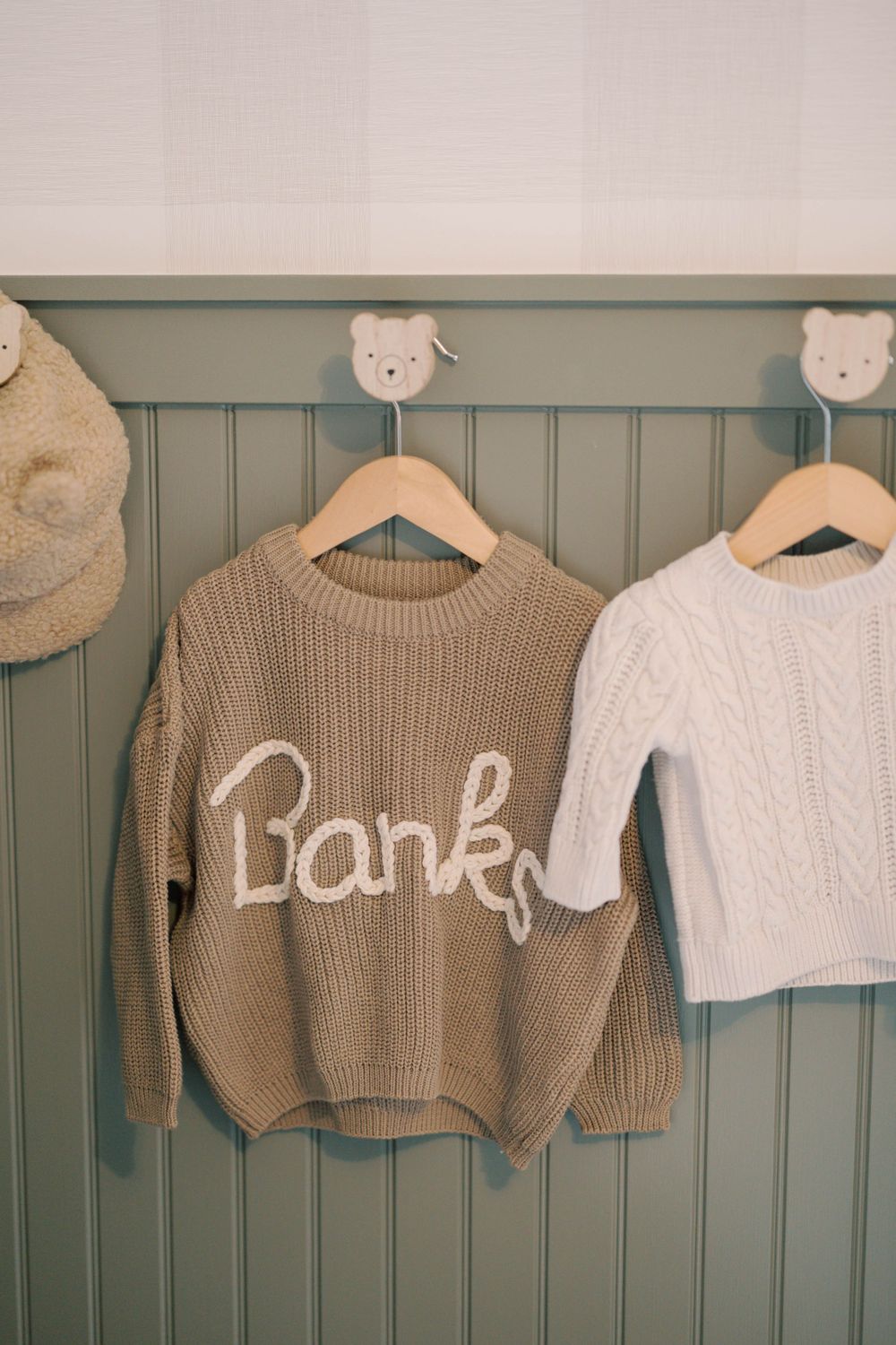 Personalized knit sweater reading Banks hanging on sage green beadboard wall with bear-shaped hooks.