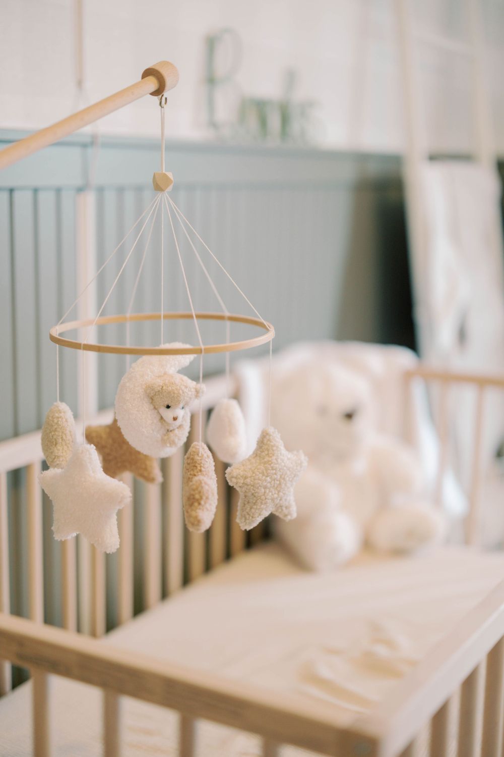 Beige nursery crib mobile featuring plush bear on moon and star shapes hanging above a wooden crib.