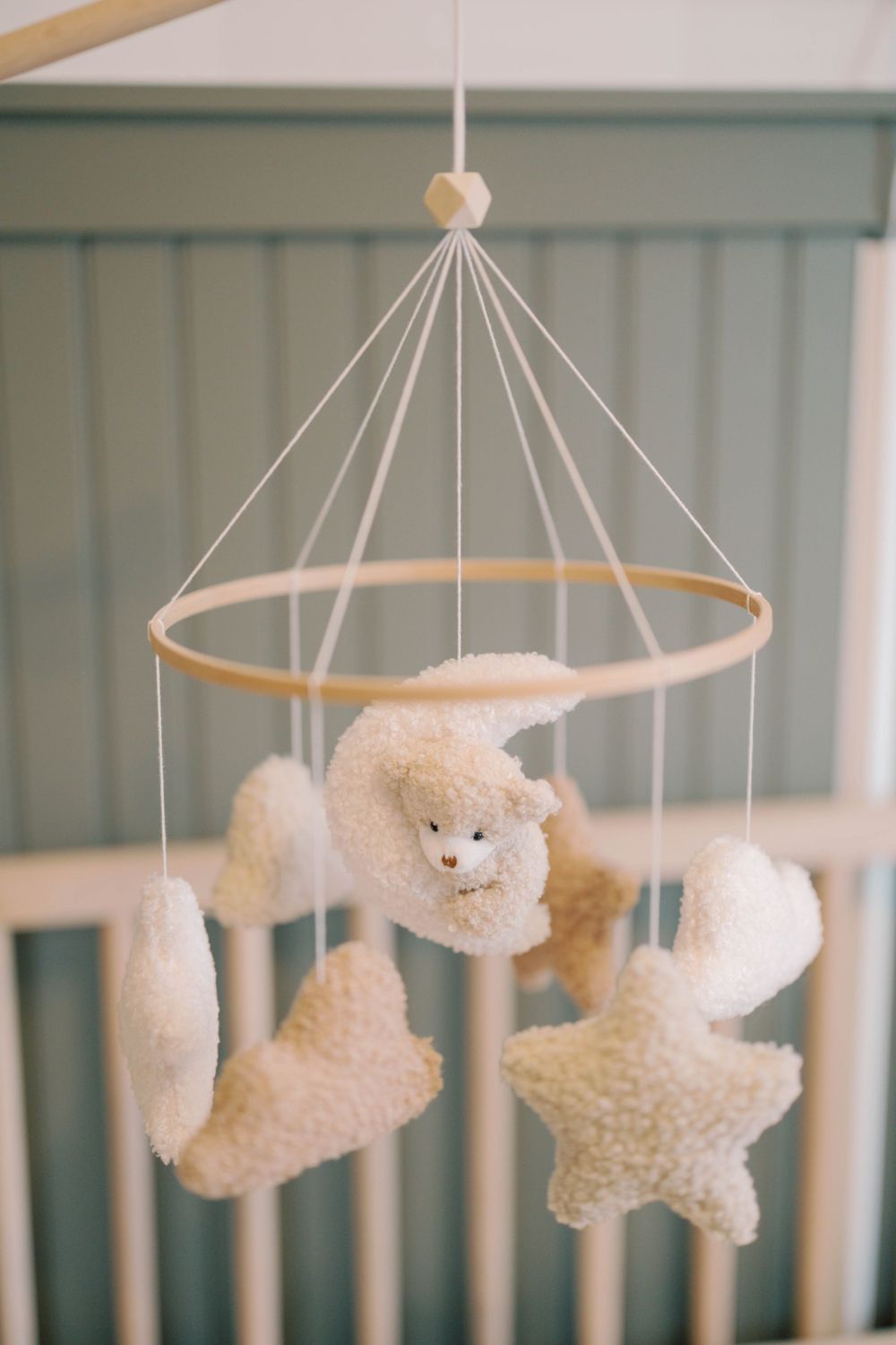 Neutral-toned baby crib mobile with plush teddy bear, moon, and star shapes hanging from wooden ring.