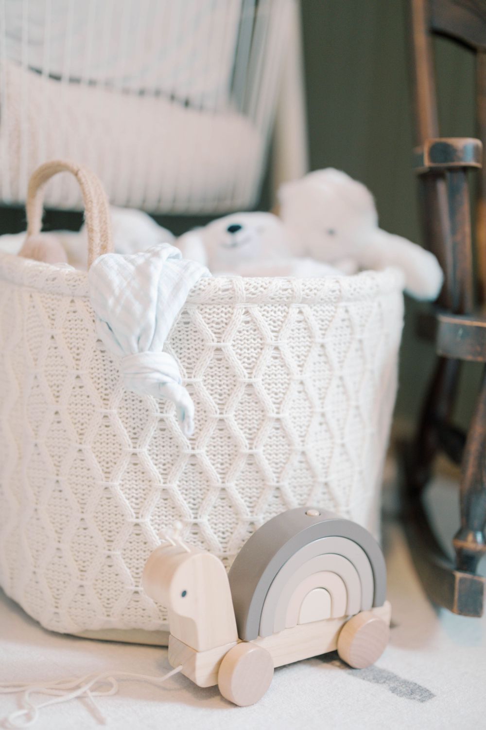 Wooden turtle pull toy beside white knit basket filled with stuffed animals in a neutral baby nursery.