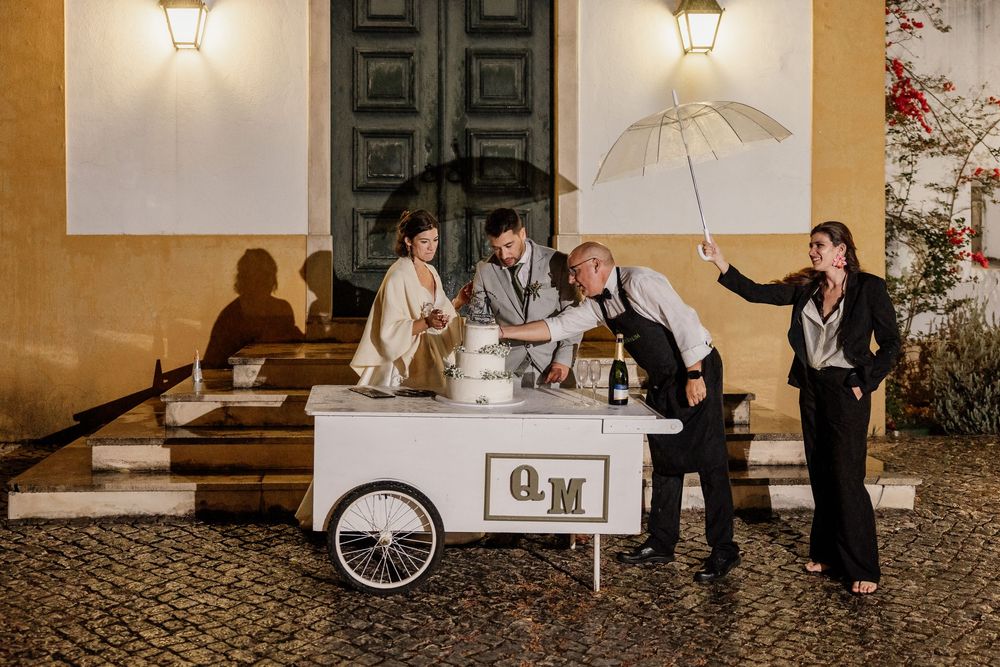 Couple with guests at a white wedding dessert cart with monogram outdoors at night.