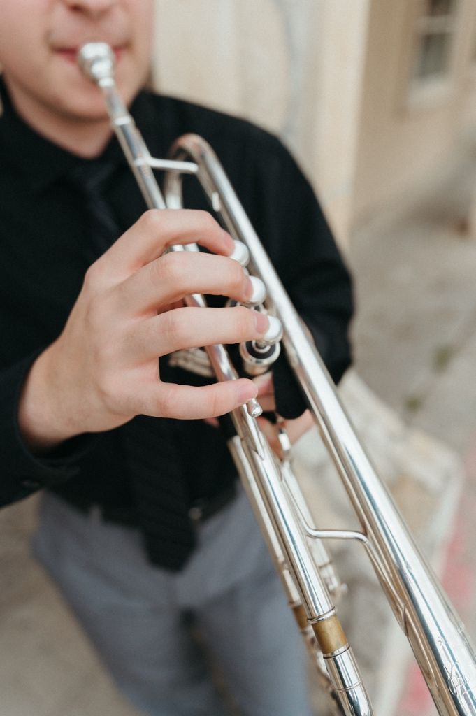 A musician in a black shirt plays a silver trumpet, fingers pressing the valves in a close-up shot.