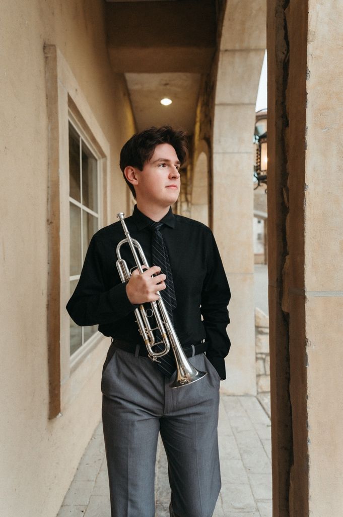 Teenage trumpet musician in black shirt and tie standing in an archway corridor.