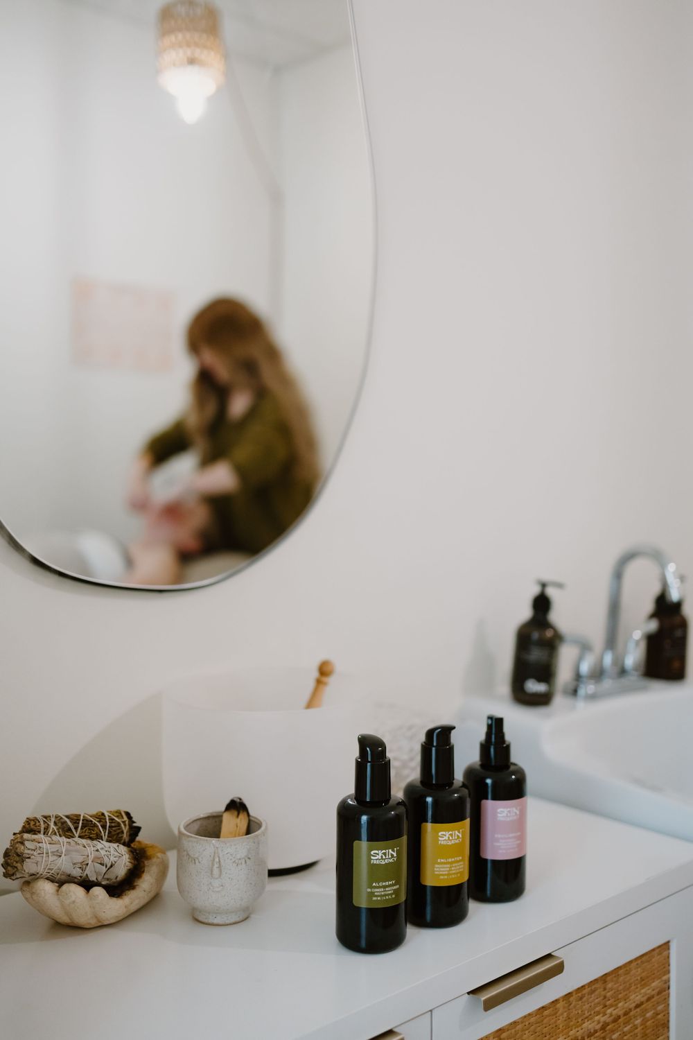 White vanity table displaying various skincare and beauty products with a round mirror.