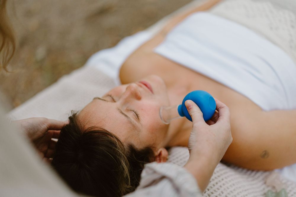 Someone lying down with closed eyes holding a small blue ball against their chest in a relaxing pose.