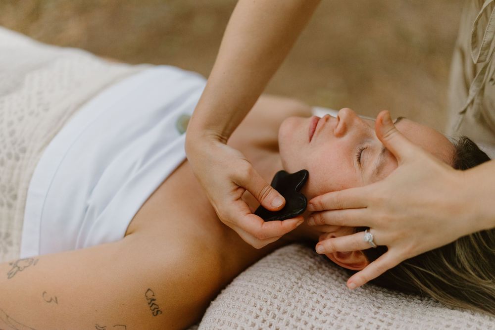 A sequence of hands performing a relaxing facial massage on someone lying down on white linens.