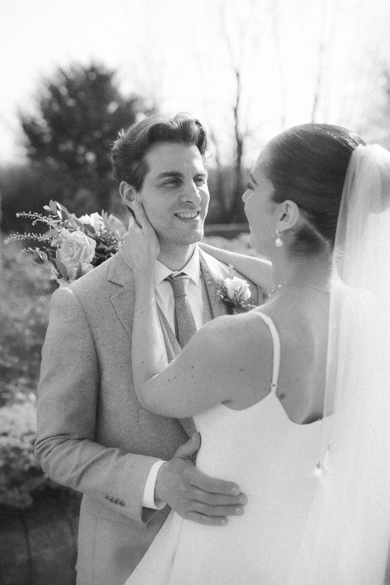 Black and white wedding portrait of a couple sharing an intimate moment outdoors with trees in the background.