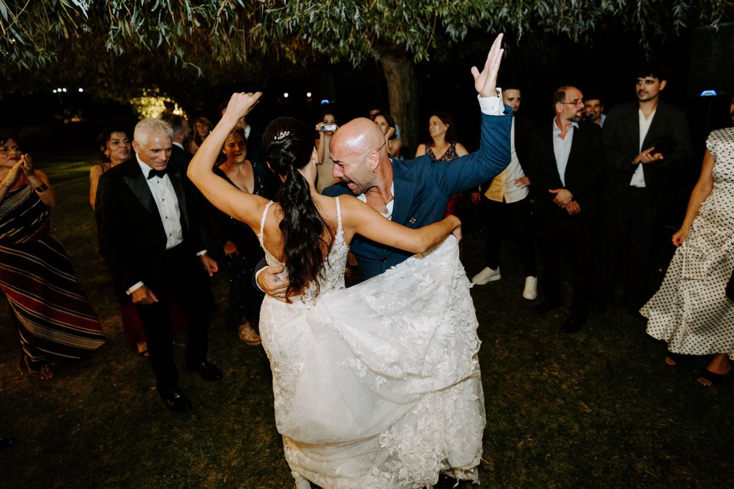 Energetic wedding reception dance floor moment with bride being dipped by guest outdoors at night.