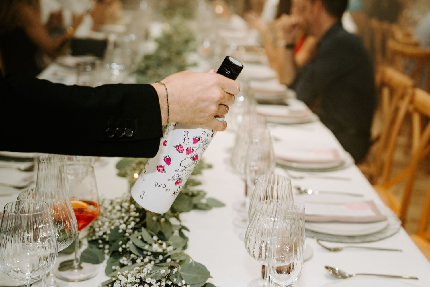 A decorated bottle of wine being poured at an elegant wedding reception dinner table.