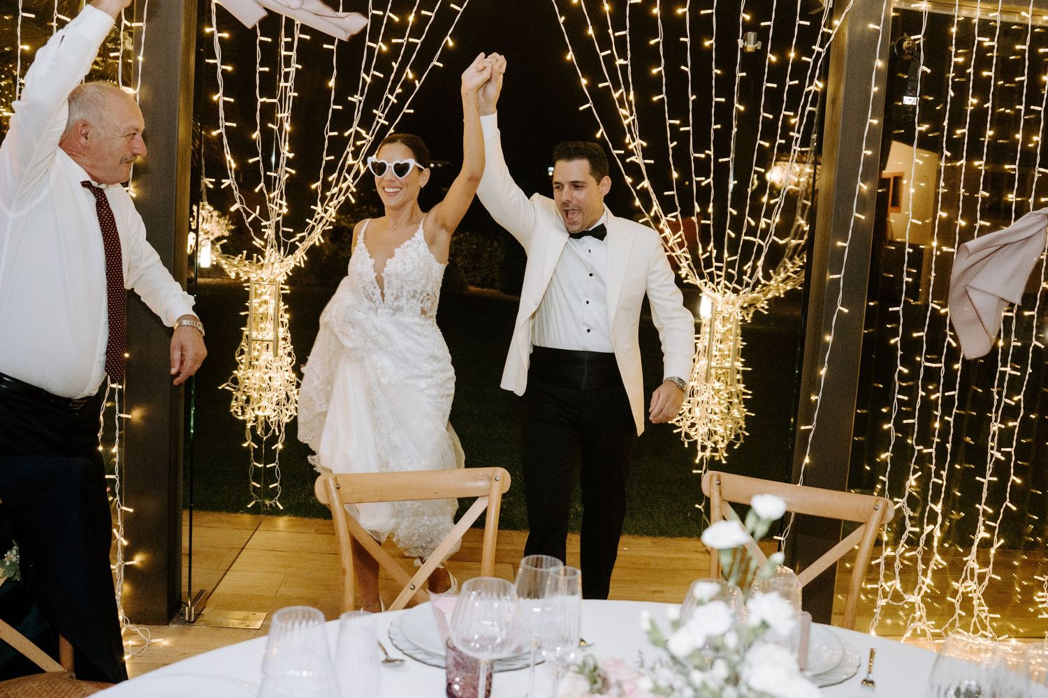 Bride and groom making grand entrance under sparkling fairy light curtain backdrop.