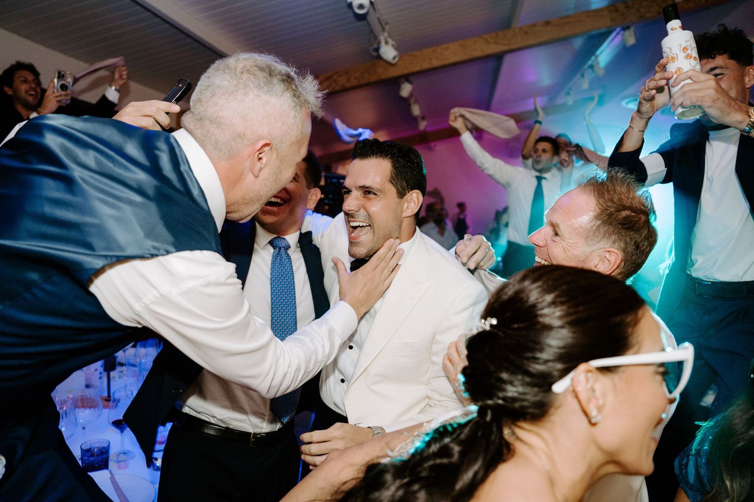Excited wedding guests lifting groom during lively celebration on the dance floor.