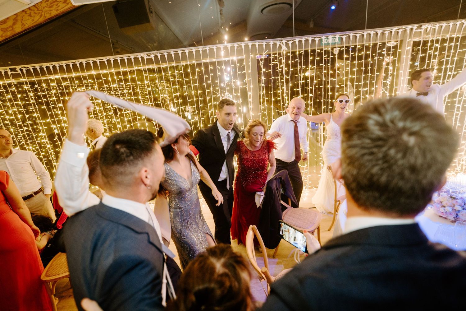 Wedding guests dancing together in front of a sparkling fairy light backdrop.