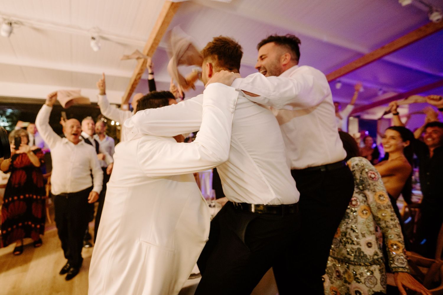 Groomsmen dancing and celebrating energetically together on the wedding reception dance floor.