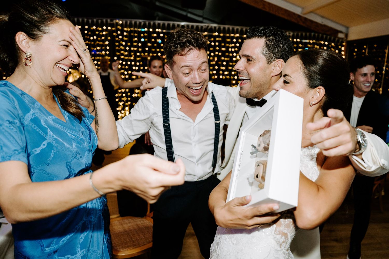 Joyful wedding guests laughing and celebrating while groom holds a photo booth strip.