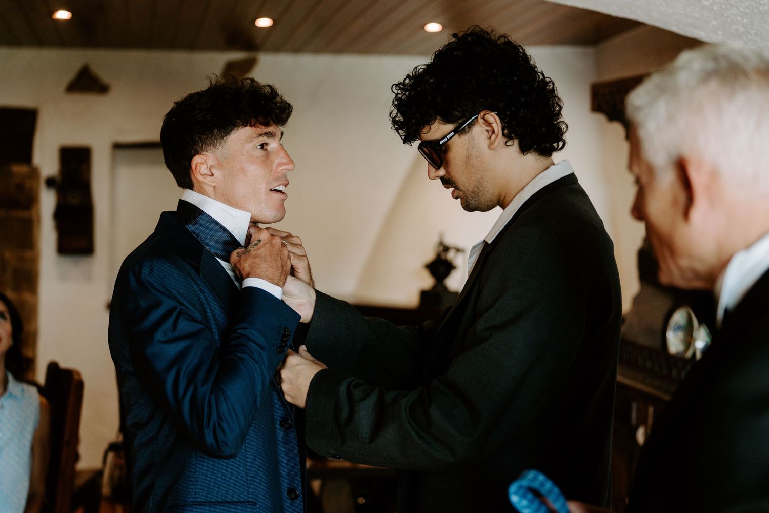 Groomsman adjusting grooms tie before wedding ceremony indoors.