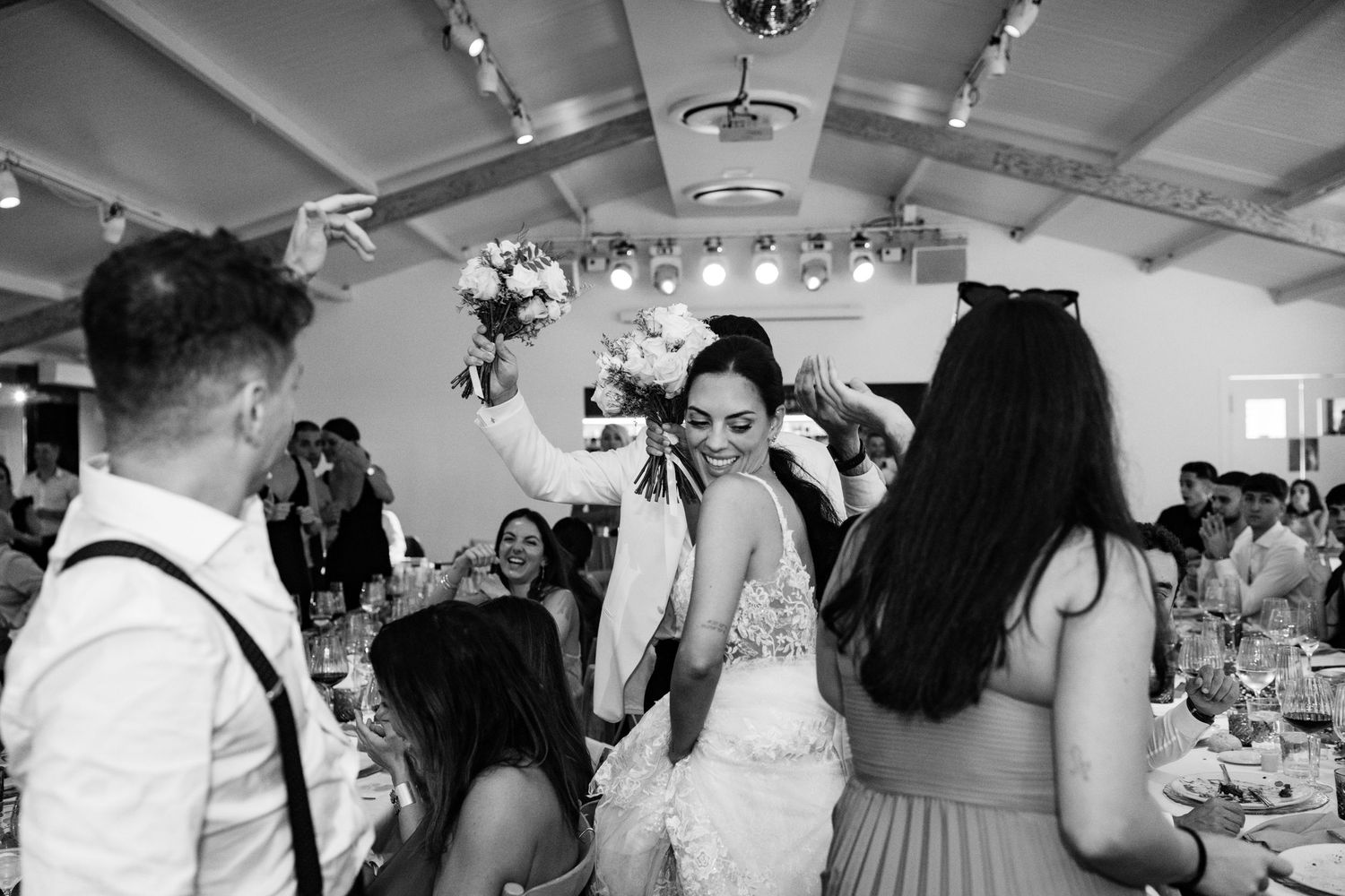 Bride dancing joyfully with guests at wedding reception in black and white photo.