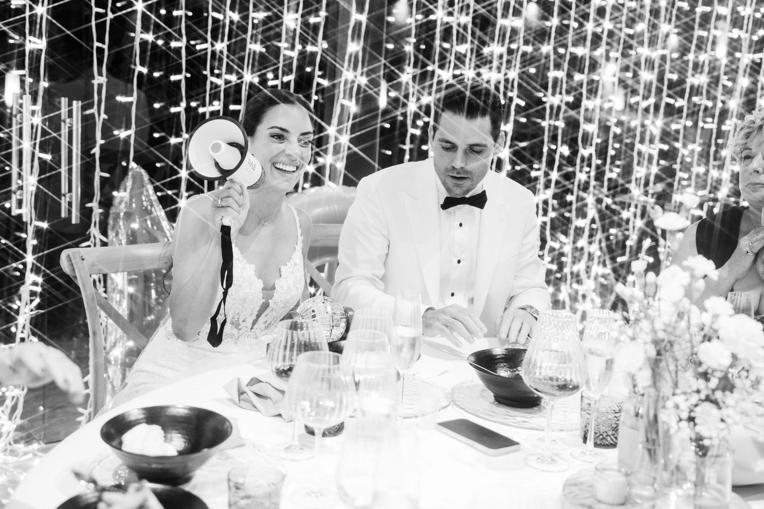 Black and white photo of bride and groom laughing at their wedding reception table.