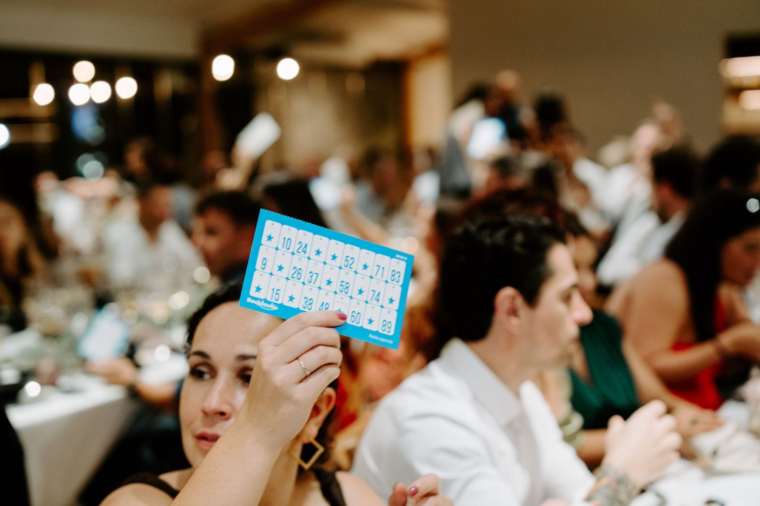 Wedding guest holds up a blue bingo card during a fun reception game activity.