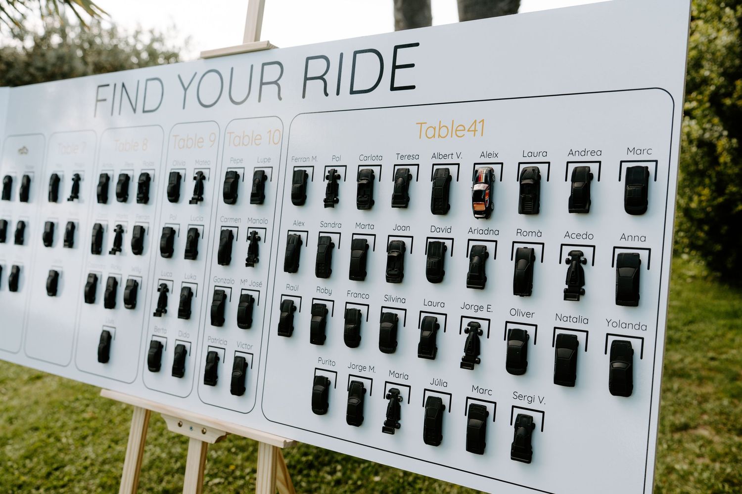 Wedding seating chart board labeled Find Your Ride displayed on easel outdoors.