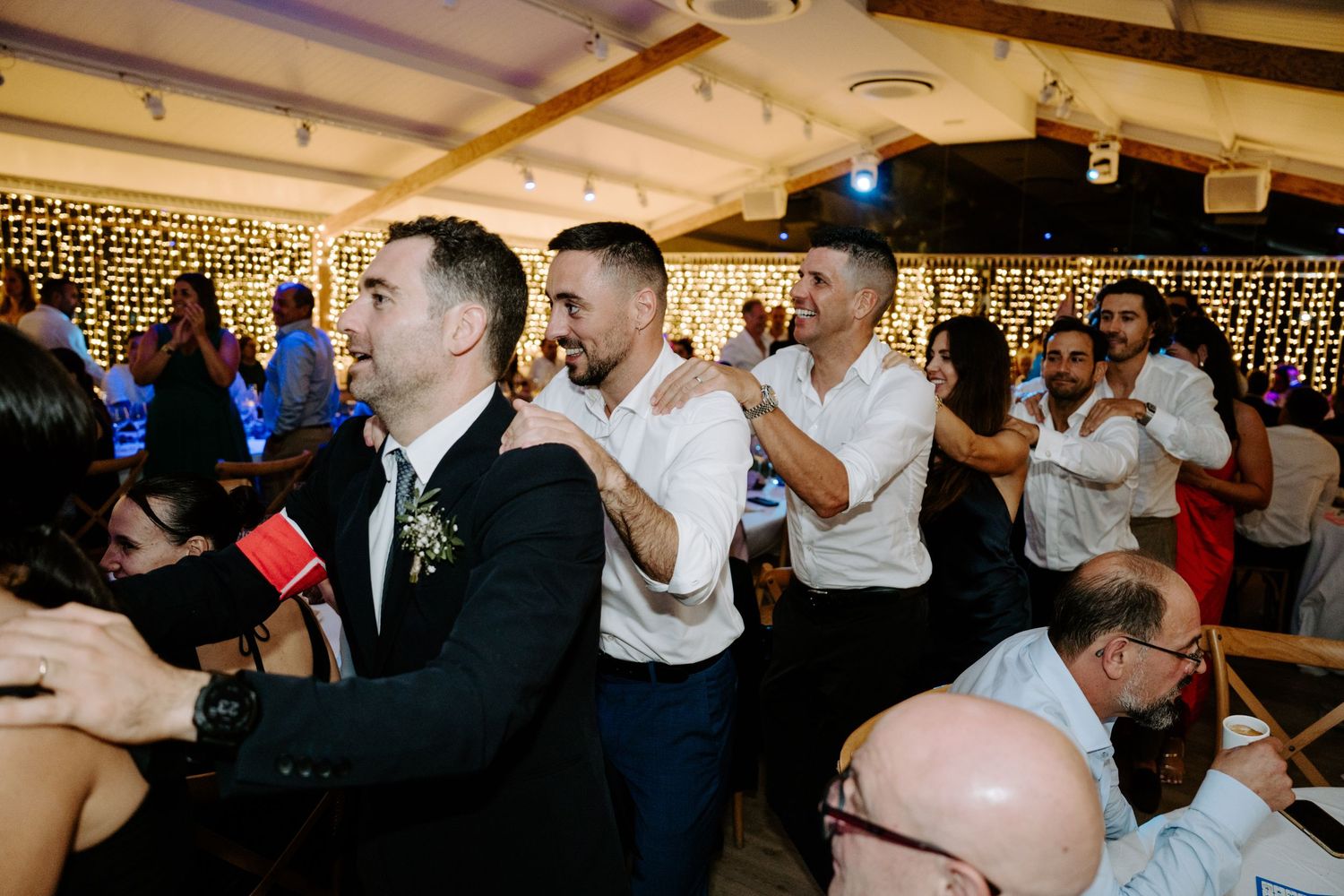 Guests dancing and celebrating at a wedding reception with fairy lights in the background.