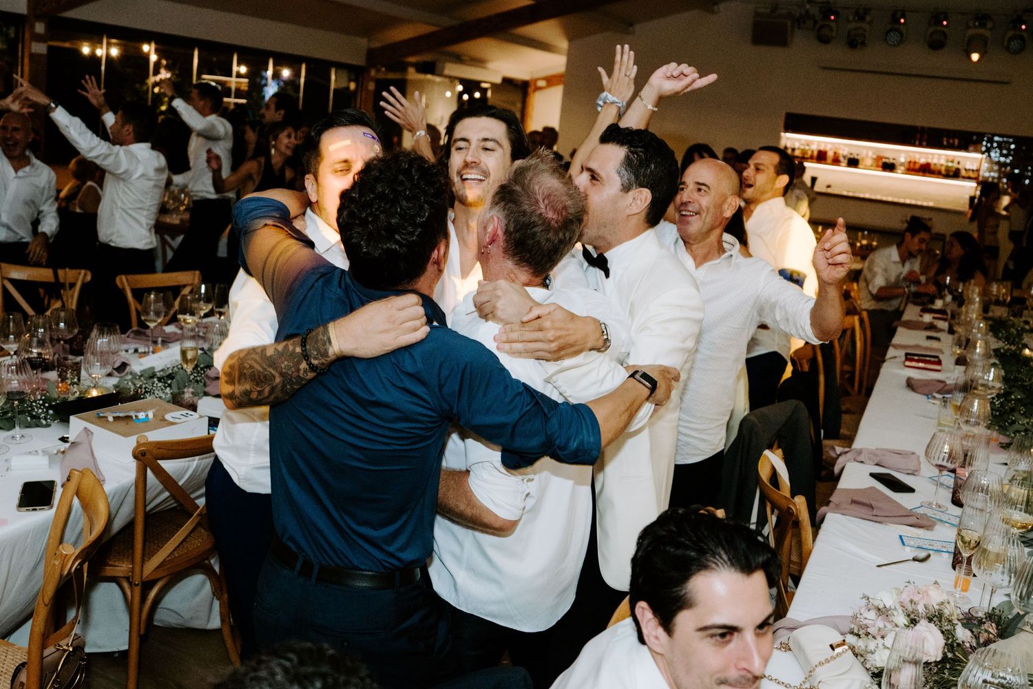 Joyful wedding guests hugging and celebrating at a decorated reception dinner table.