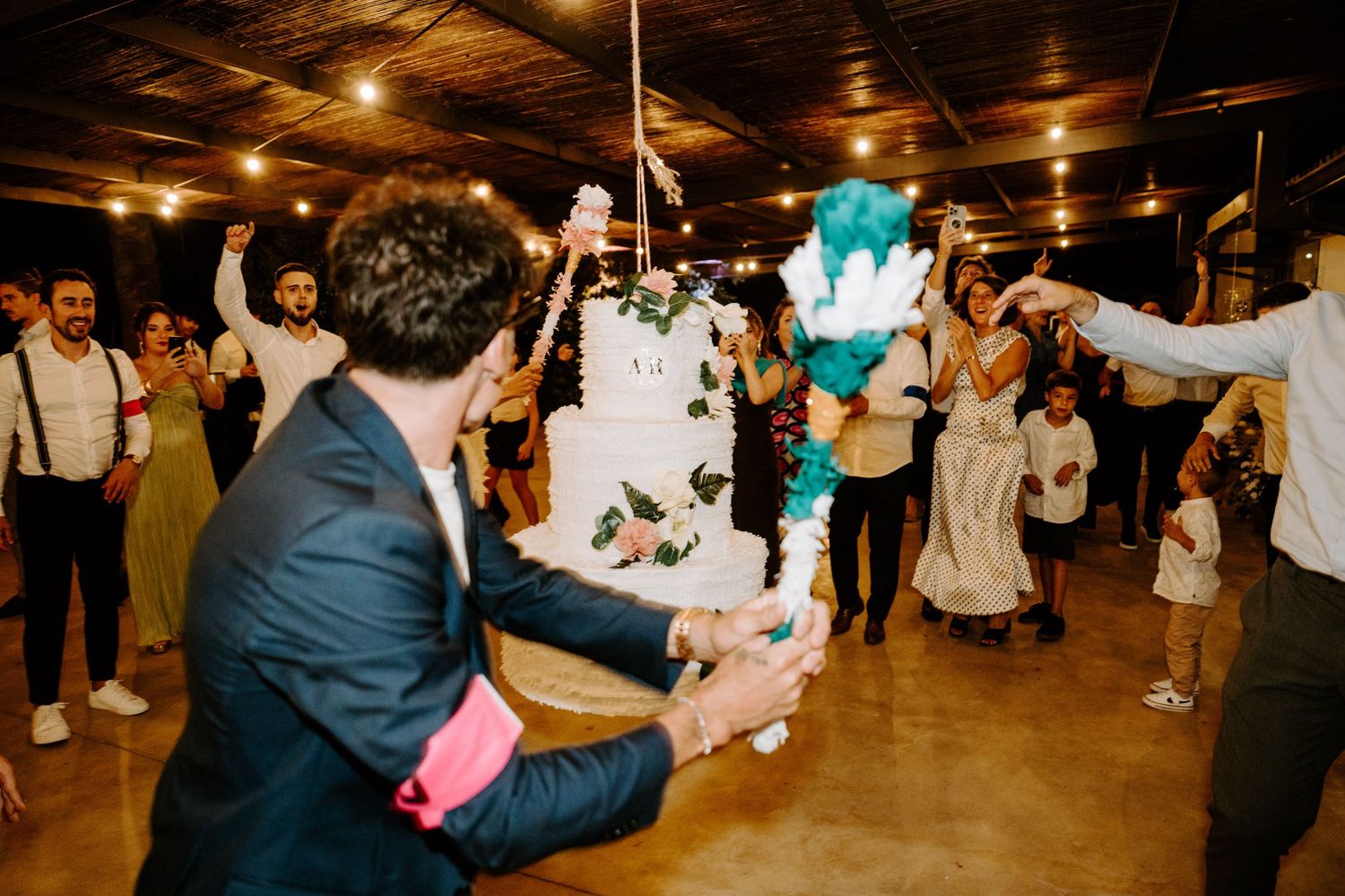 Guests celebrating around a white wedding cake with teal floral decorations on the dance floor.
