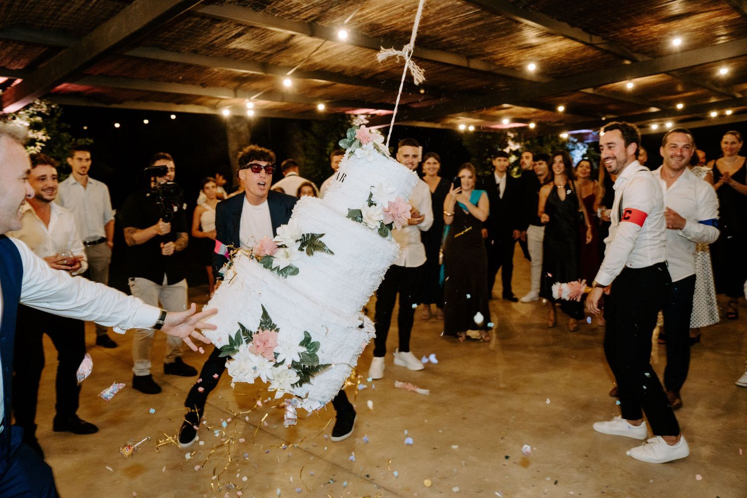 Guests smashing a floral wedding piñata at a festive indoor reception celebration.