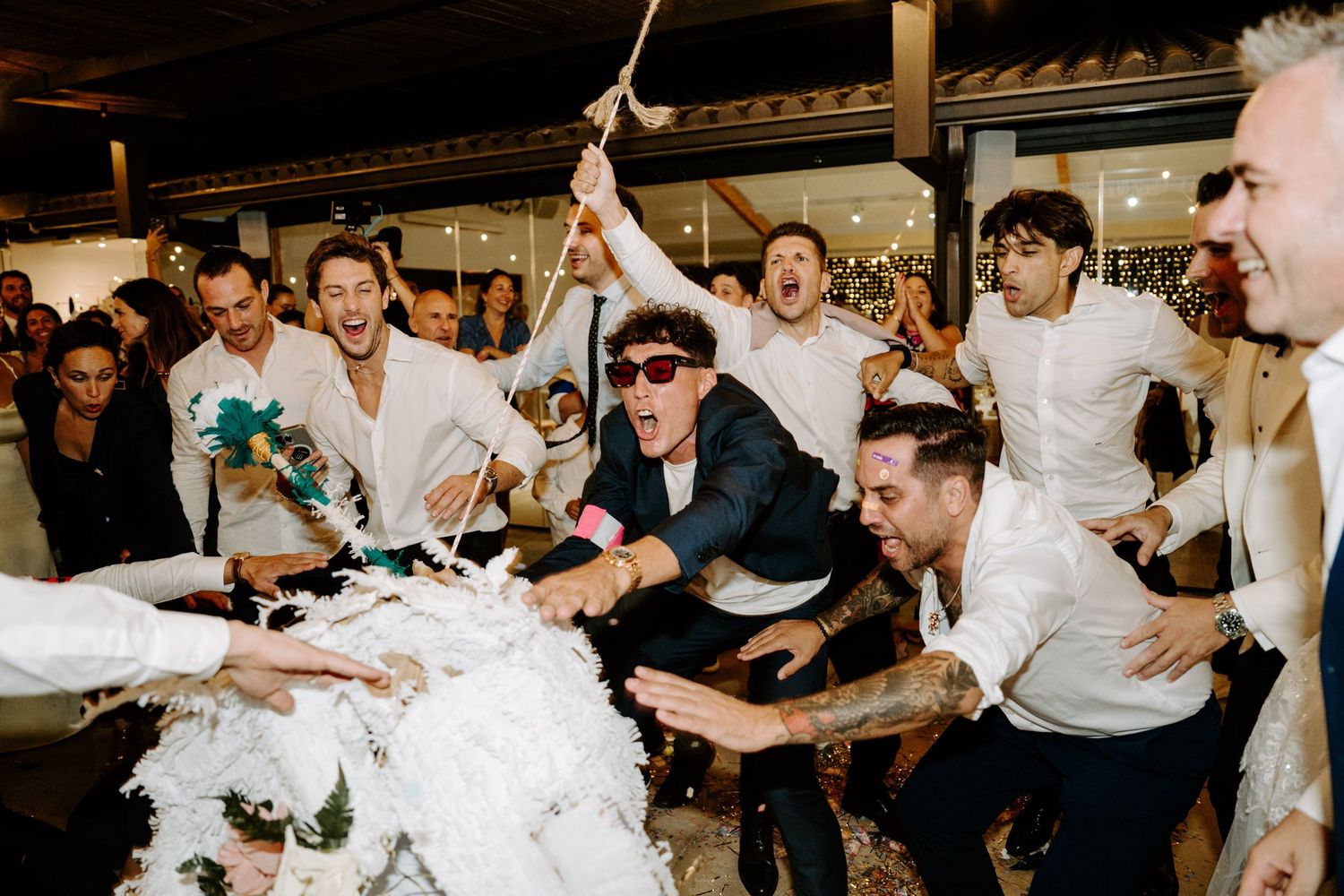 Groomsmen excitedly smashing wedding cake together at outdoor reception celebration.