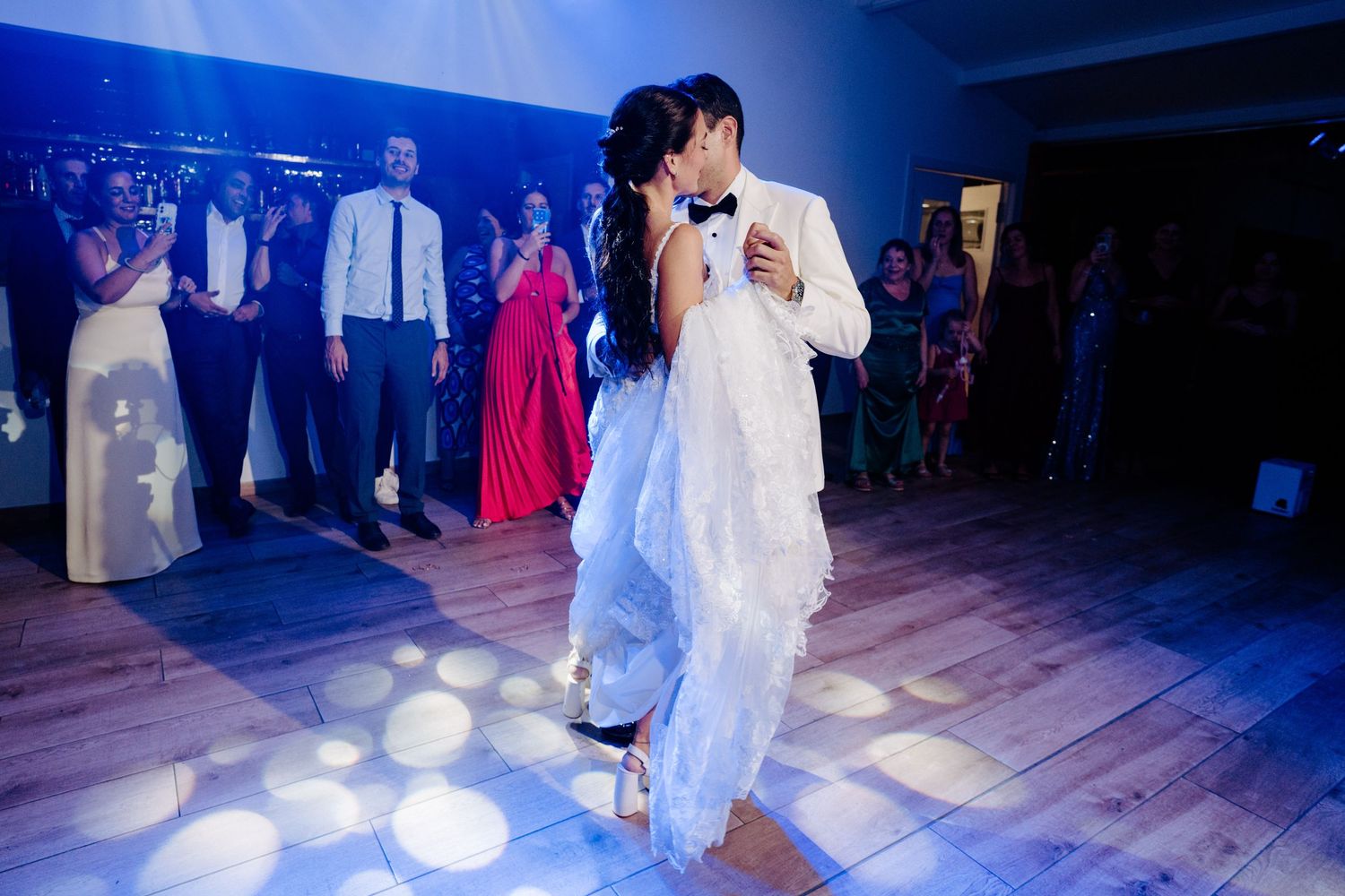 Bride and groom share romantic first dance surrounded by guests at wedding reception.