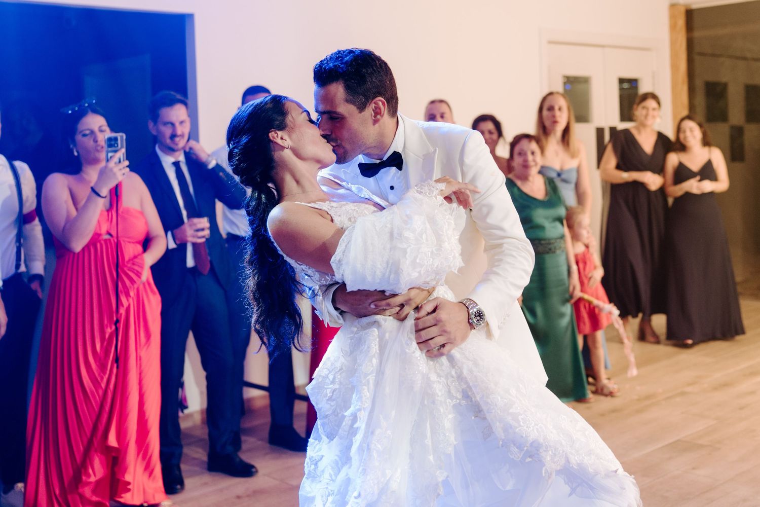 Bride and groom sharing a romantic first dance kiss in wedding attire before guests.