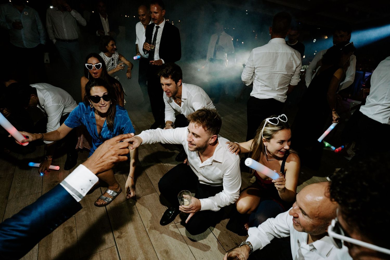 Wedding guests dancing and celebrating on a smoky outdoor dance floor at night.