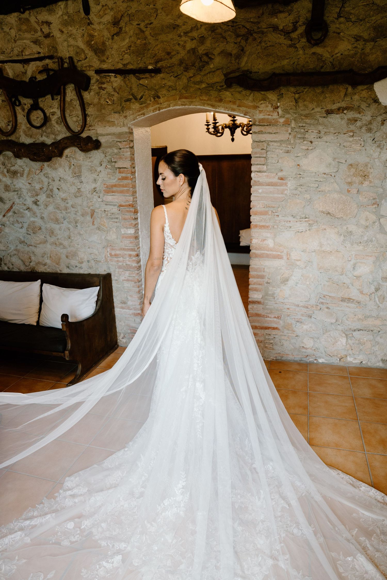 Bride in stunning white lace gown with long cathedral veil in stone venue.