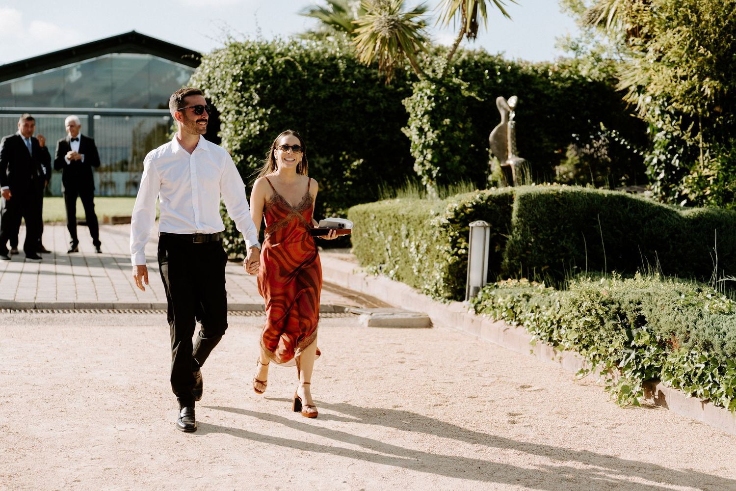Couple walking hand in hand through scenic garden venue on wedding day.