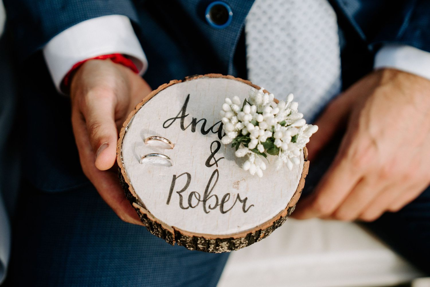 Ring bearer holding wooden slice with Ana and Rober wedding rings and flowers.