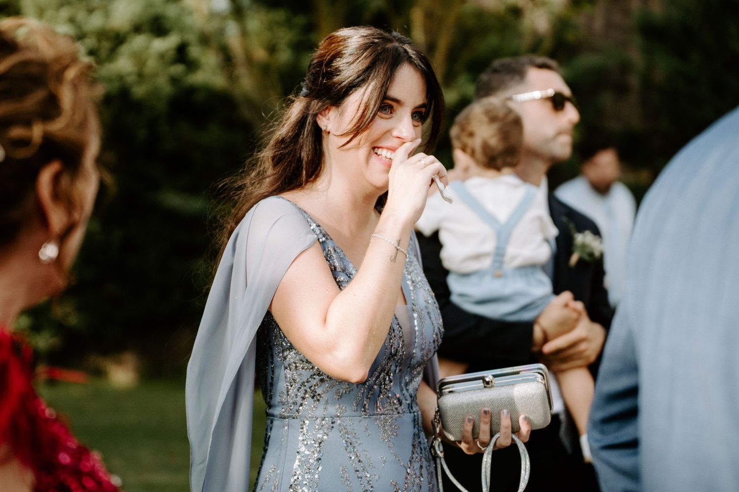 Elegant wedding guest in a beaded blue gown smiling warmly at an outdoor garden reception.