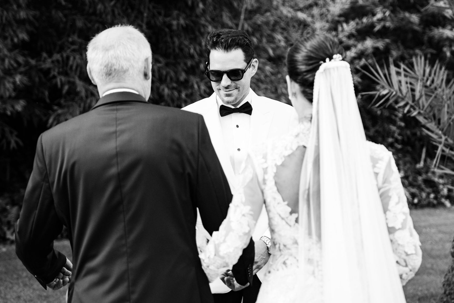 Black and white photo of groom in sunglasses seeing bride at wedding altar.